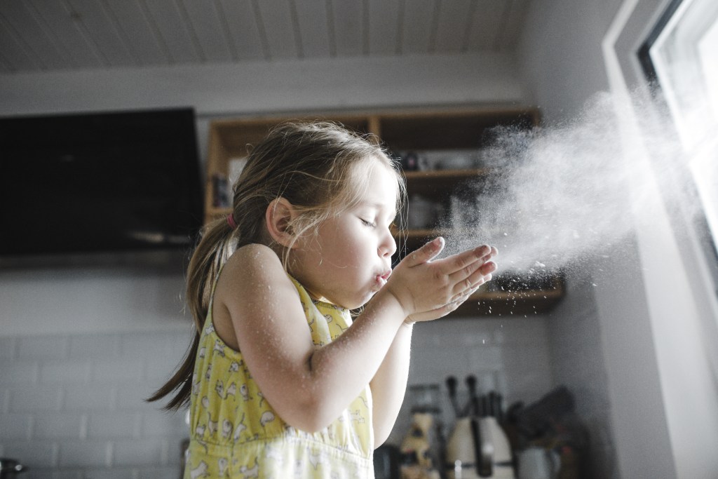 The power of breathing: Little girl blowing flour in the air in the kitchen