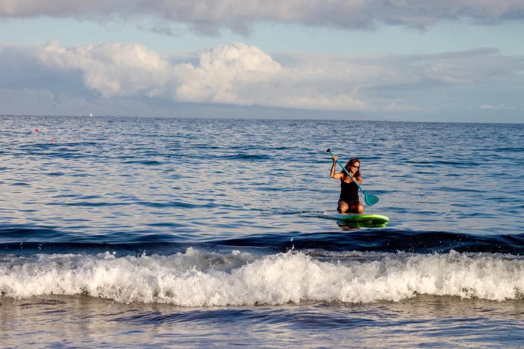 Tackling Eco-Anxiety outdoors: Young woman kneeling on surfboard and paddling towards the shore