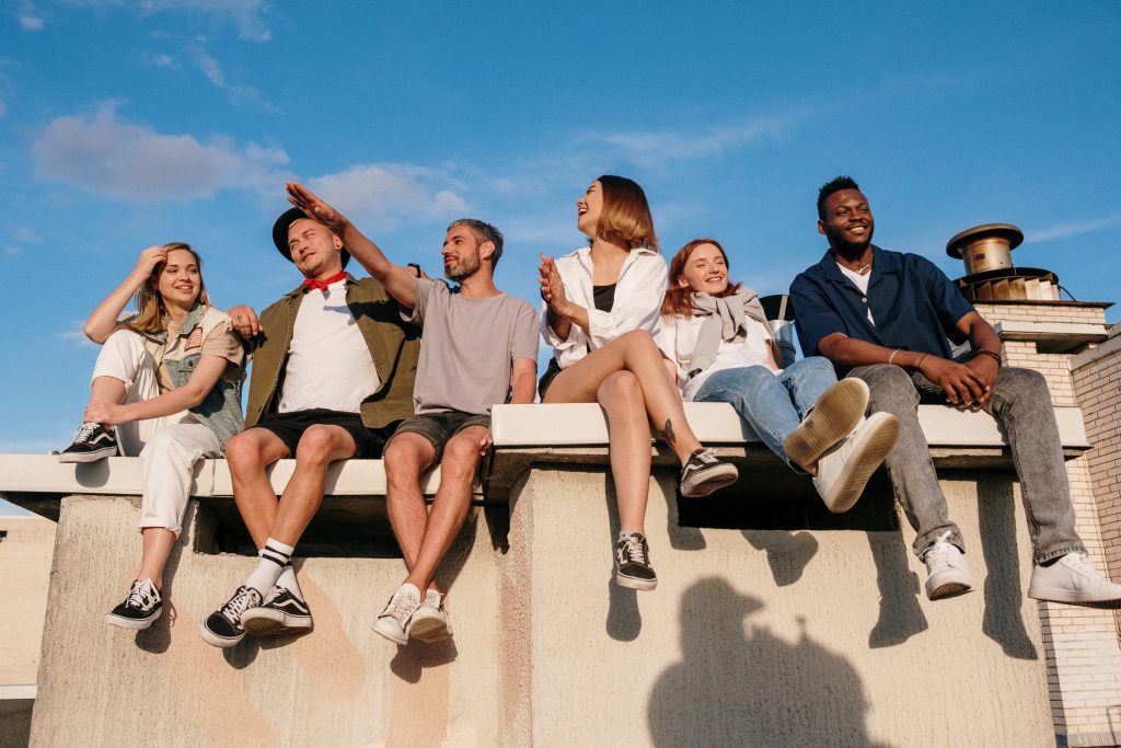 Finding hope in community: Group of 3 female and 3 male friends hanging out with each other outside. They sit on a wall with blue sky above them.