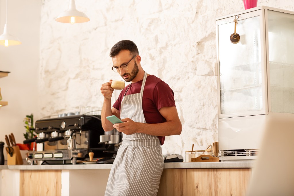 Young professional checking his Earkick stats on his smartphone while enjoying his cappuccino