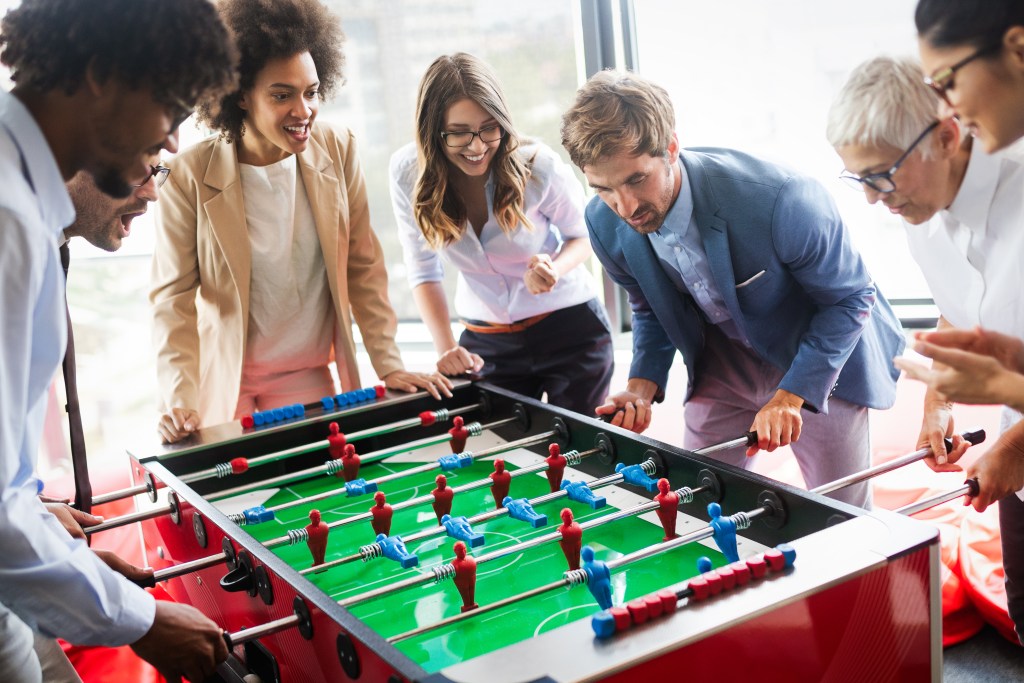 Employees playing table soccer indoor game in the office during break time to bond with each other and relieve stress 