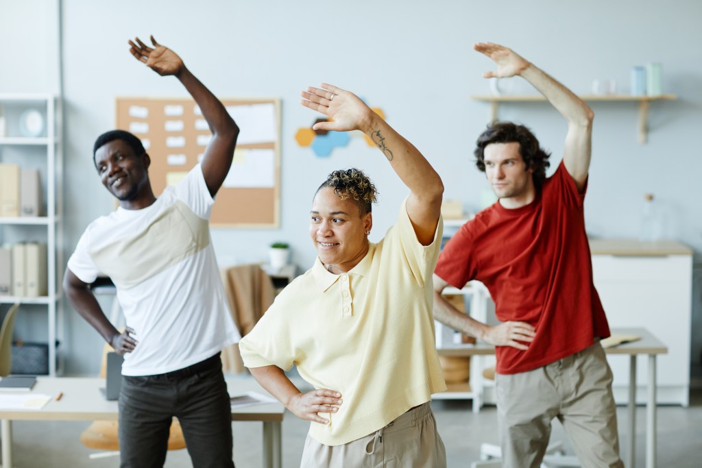 Group of employees doing stretching exercises in between meetings at the office