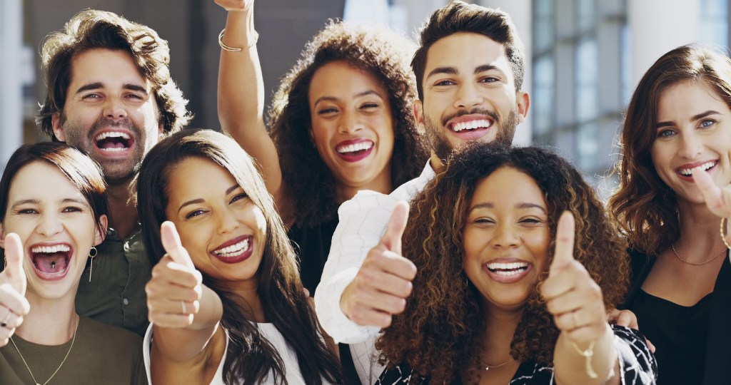 Group of 5 females and 2 male young business people giving thumbs up for their workplace that prioritizes mental health and supports mental readiness via actionable strategies. 