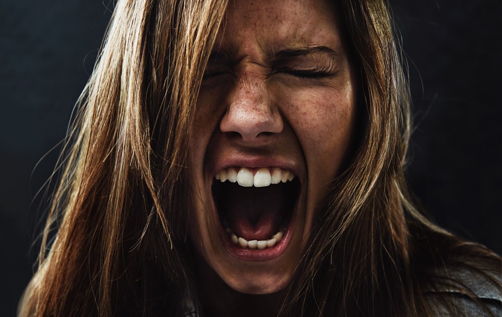 Intense emotions: A young woman screaming while isolated on a black background.