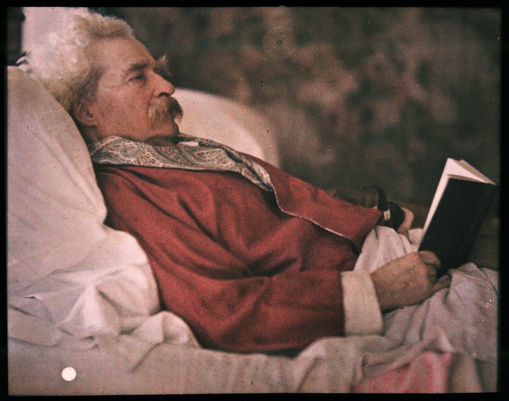 Mark Twain, American writer, humorist, and lecturer, lying in his bed with a journal and smoking his pipe. Twain kept a journal as a way to record his daily experiences, observations, and ideas. 