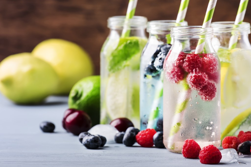 Hydration can be delicious and refreshing: Summer drinks set with berry, fruit, citrus and ice cubes in glass bottles