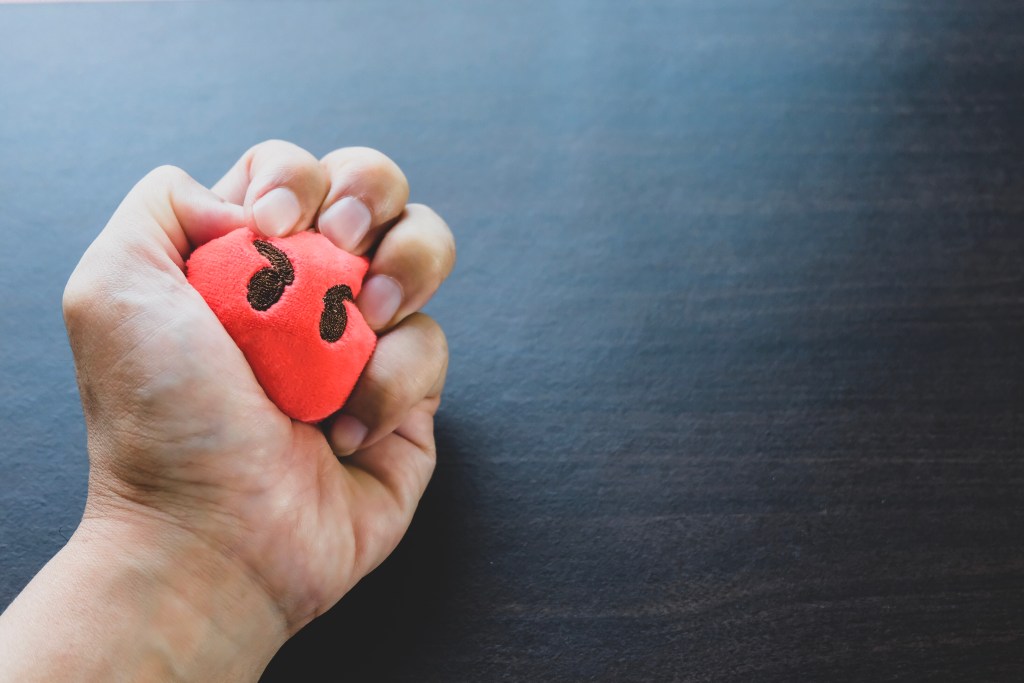 Stress, anxiety, fear and worry are common emotions experienced at the workplace: Hand crushing a red stress ball with an angry face.