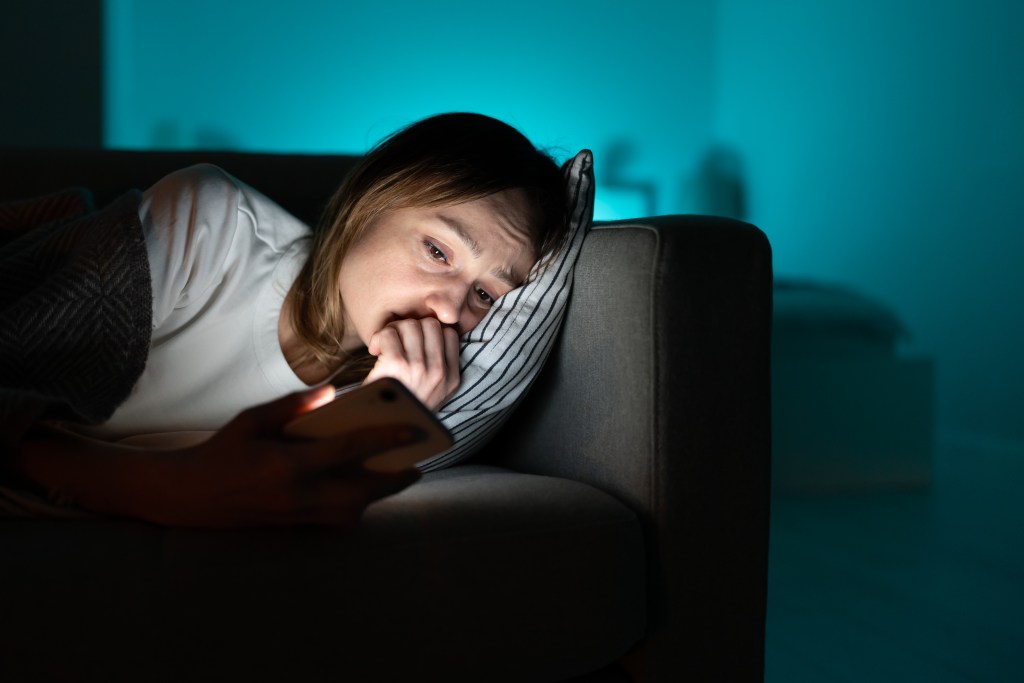Unhealthy comparison: sleepless young woman scrolling through social media on smartphone, feeling anxiety, sadness, apprehension.