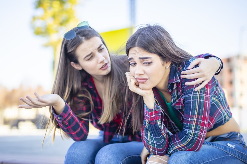 Let go: Young woman comforts her sad female friend in the park, helping her to process her feelings and let go of her ex
