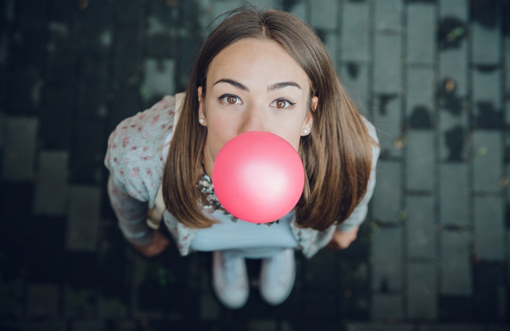 Popping the fantasy bubble: Top view of young woman blowing a pink bubble gum