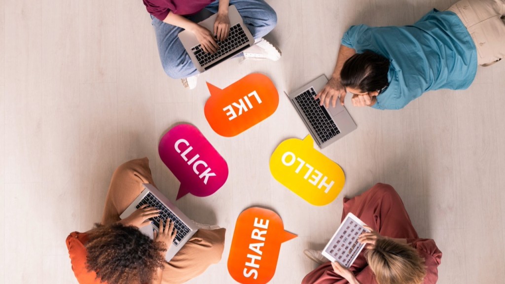 Fear of missing out (FOMO), losing out or better options (FOLO, FOBO): three young females and one male sitting on the floor, glued to their devices laptops. They share, like, chat and click away.