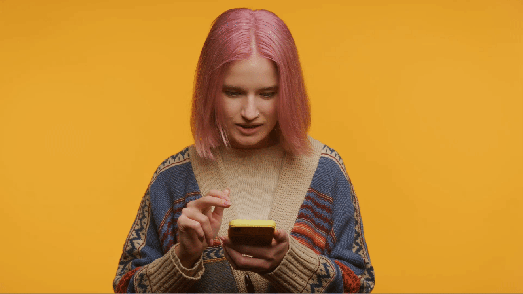 The news of a potential TikTok ban catches a young woman with pink hair by surprise. She's looking shocked while swiping on her smartphone and shaking her head.