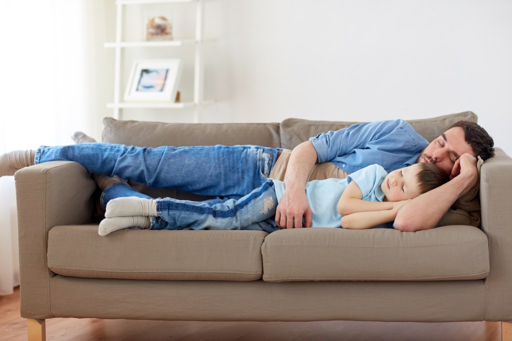 Single dad and little son sleeping on sofa at home. He uses a personal AI chatbot for mental health