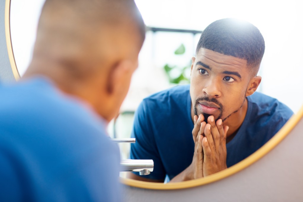 Glow up culture: Young man admiring his face in the mirror after successful skin care routine