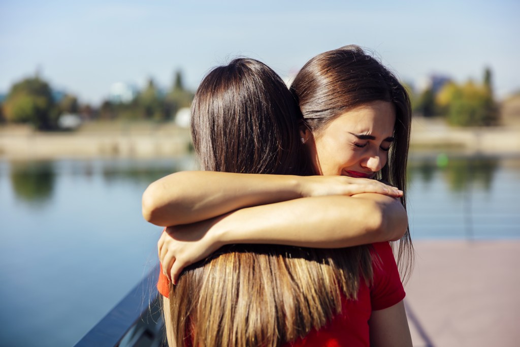 Self harm scars: Young woman hugging and supporting her best friend on the lakeside