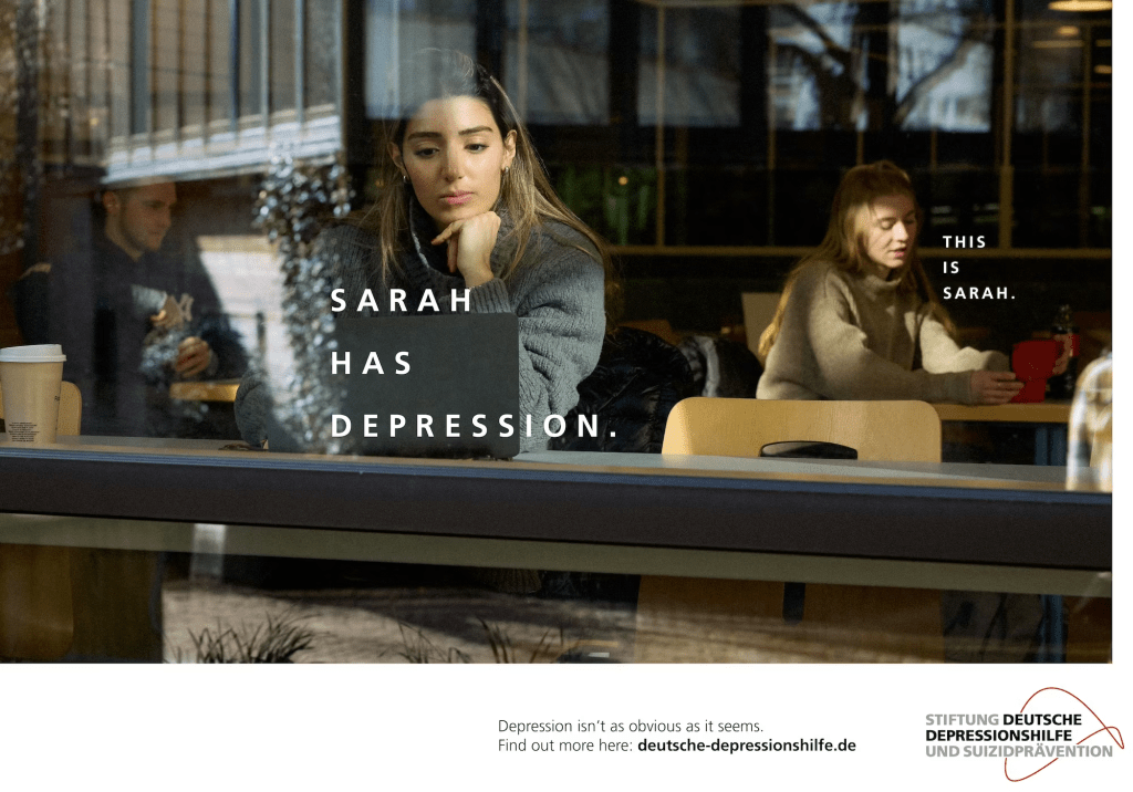 Suicidal thoughts and depression are subject to many assumptions: Young woman sitting in front of a laptop looking sad. In the background there is another woman, Sarah, who has depression, but doesn't look like it. (Campaign to challenge assumptions around depression and suicidal thoughts by Stiftung Deutsche Depressionshilfe und Suizidprävention)