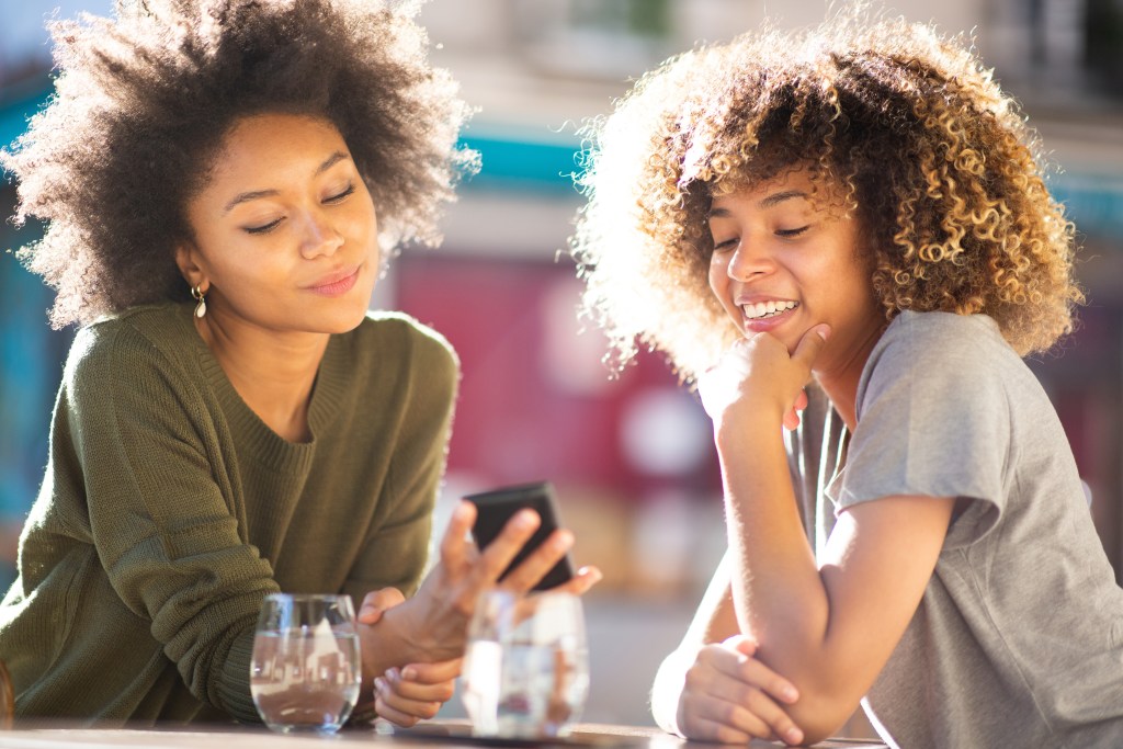 Young professional meeting a friend and showing her the progress she made with an AI in mental health.