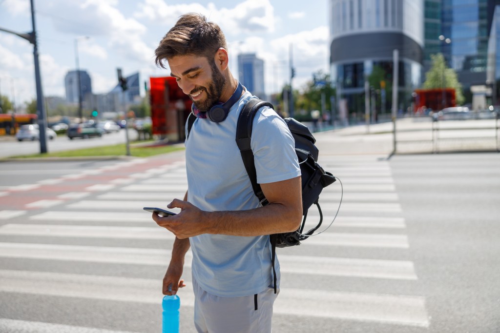 AI in mental health: Young professional being reminded by an AI to take a break from work and go for a short walk outdoors. He is interacting with his AI coach, smiling and looking at his smartphone.