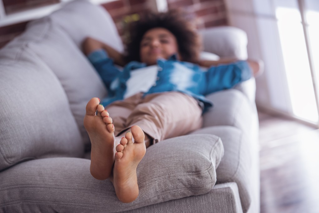 A person who has learned all about the psychology of creative burnout taking a rest on the sofa with their feet up high.
