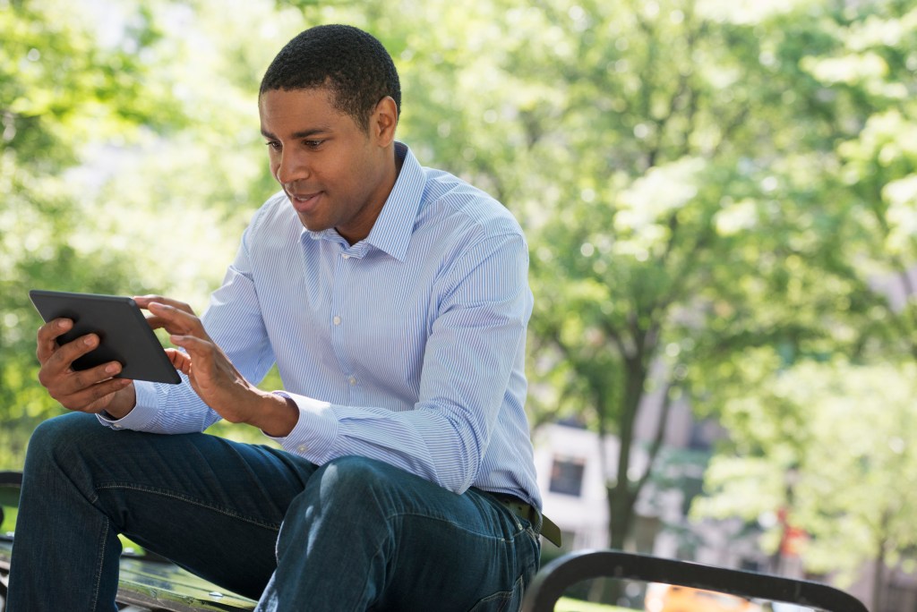 AI mental health tracking at work: Summer in a city park, businessman sitting using a digital tablet to check his mental health data.