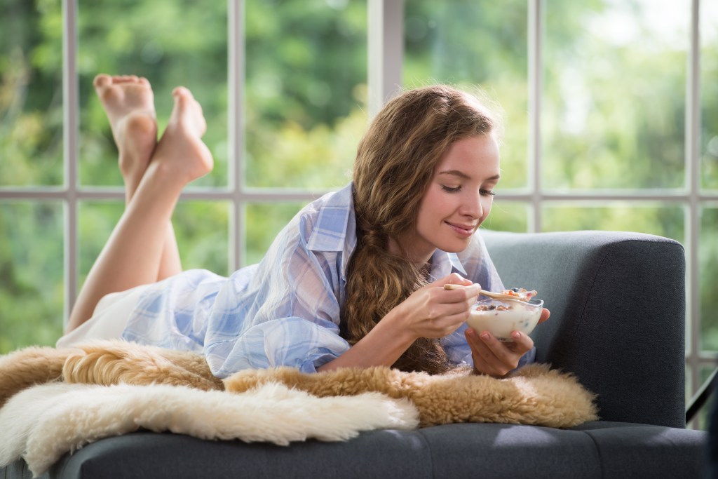 Combatting crippling anxiety: Woman lying on couch eating a bowl of greek yogurt