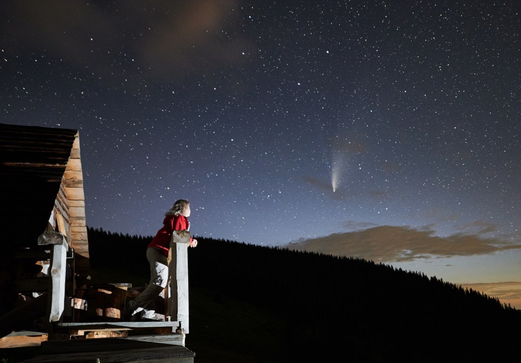 When life feels impossible: Woman watching beautiful starry night and a comet from a her porch