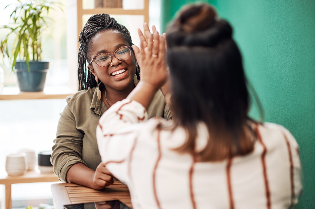 "Girl, I've got your back." Shot of two young women giving each other a high five in a cafe