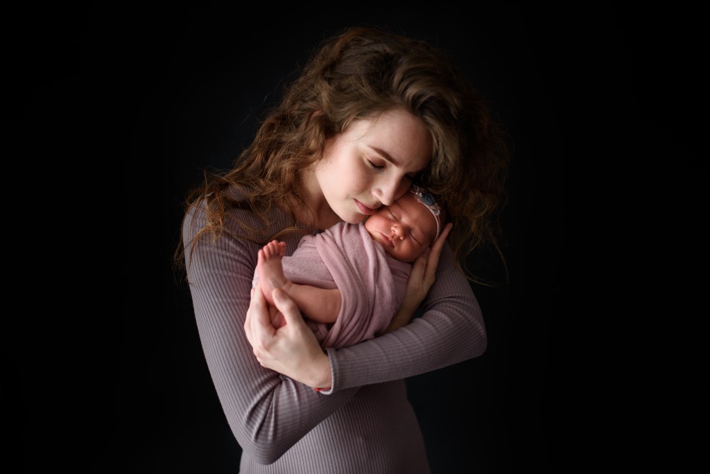 New mom is holding her newborn daughter. Picture taken on a dark background.