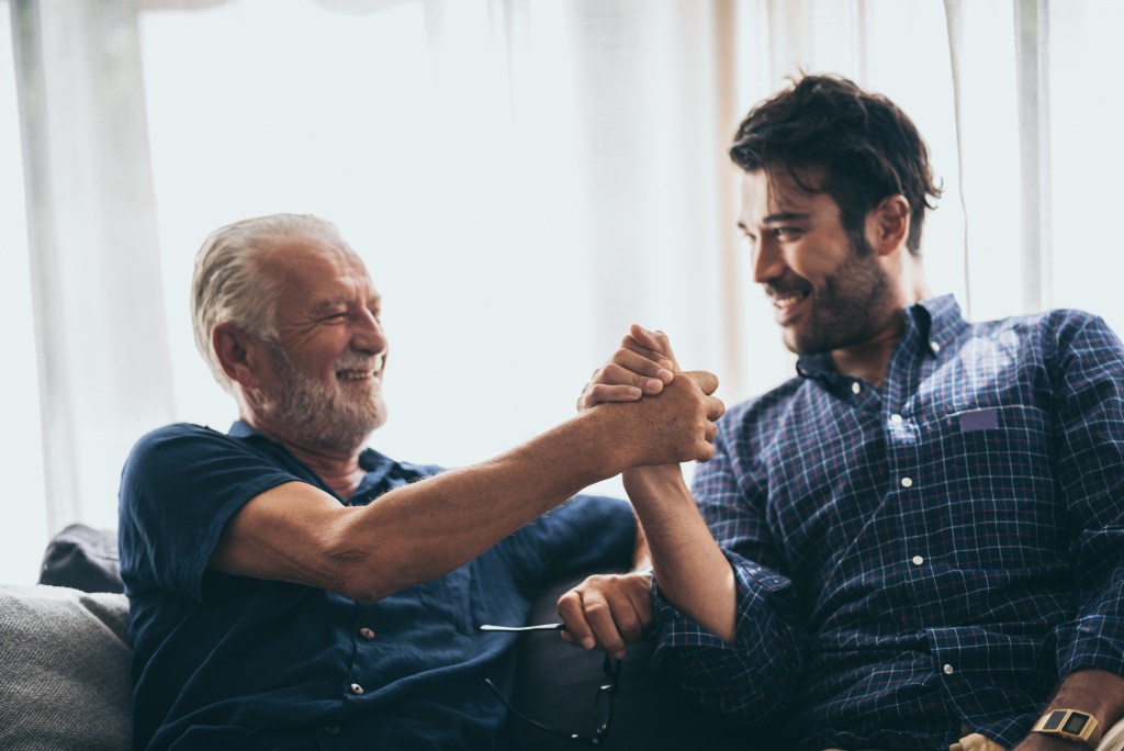 Father-son relationship: Cheerful elderly man sitting on the sofa next to his adult son
