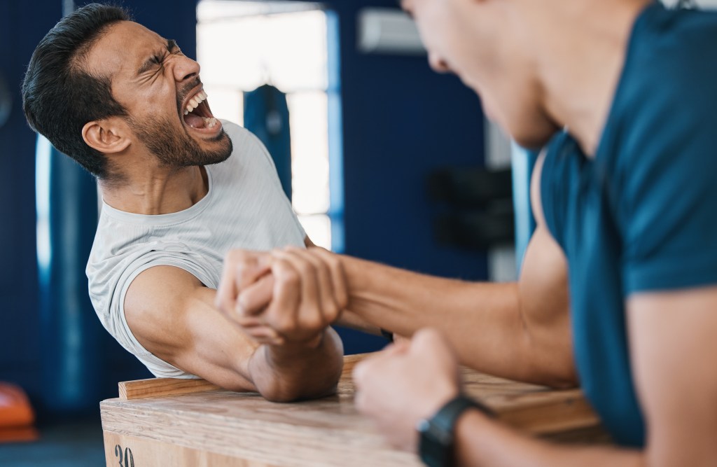 Men’s mental health quotes: Men arm wrestling on a table in playful challenge.