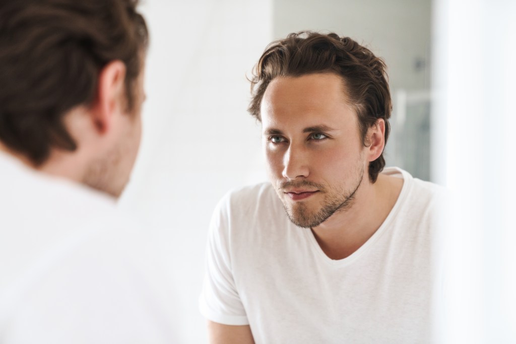 Men’s mental health quotes: Confident man standing in front of a mirror, looking at himself
