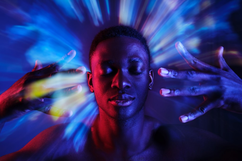 When should someone talk to a mental health professional about unwelcome thoughts or emotions? Man holding hands near face while standing with eyes closed in blurred blue lights 