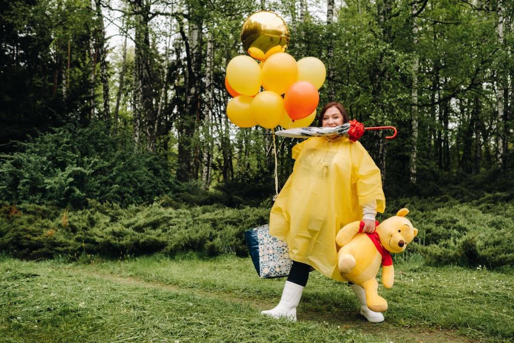 Winnie-the-Pooh Mental Illness Theory: Woman in a yellow raincoat holding Pooh and many different things.
