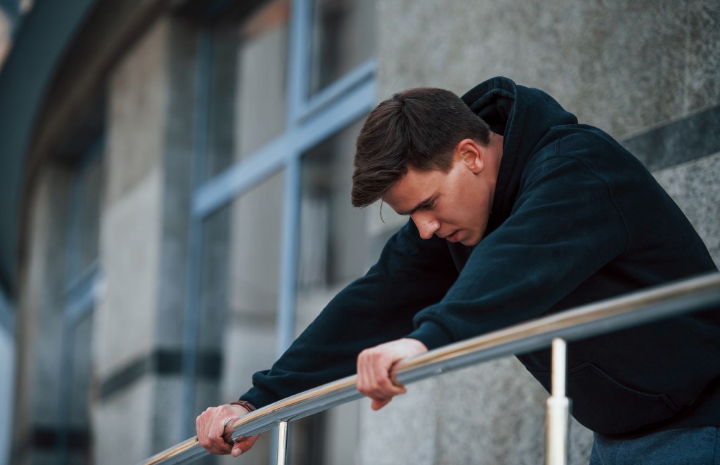 Recovering young man leaning on the silver colored railings recalling positive mental health quotes 