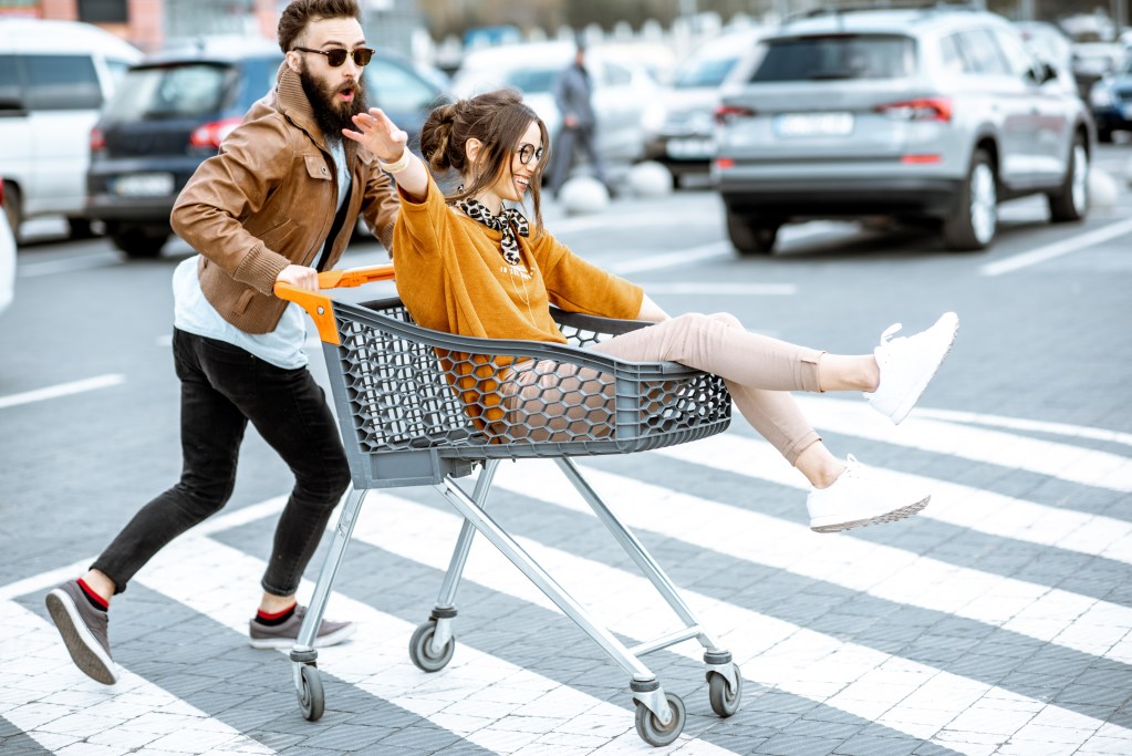 Dating someone with ADHD: couple having fun riding with shopping cart on the outdoor parking 