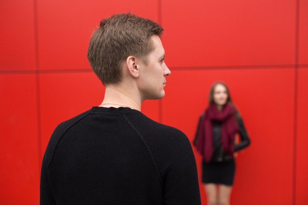Why Do I Have Commitment Issues? Couple on the street with a backdrop of the red wall. 