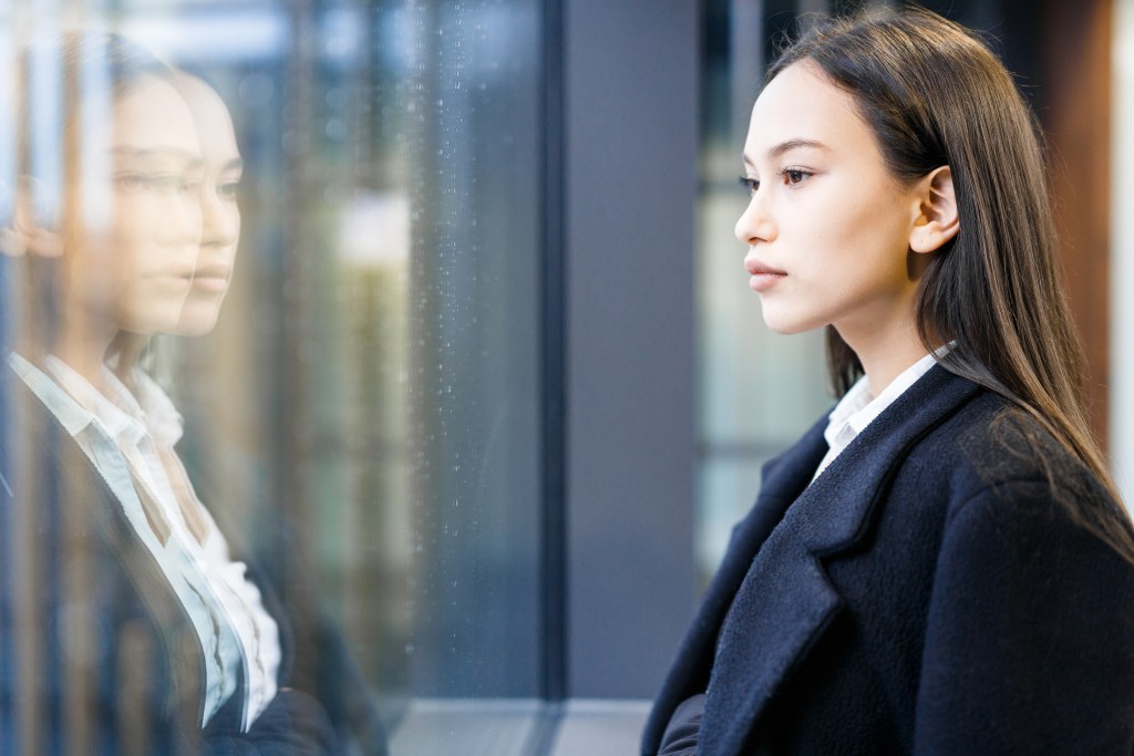 Why Do I Have Commitment Issues? Young professional reflecting on her patterns while looking through office center window