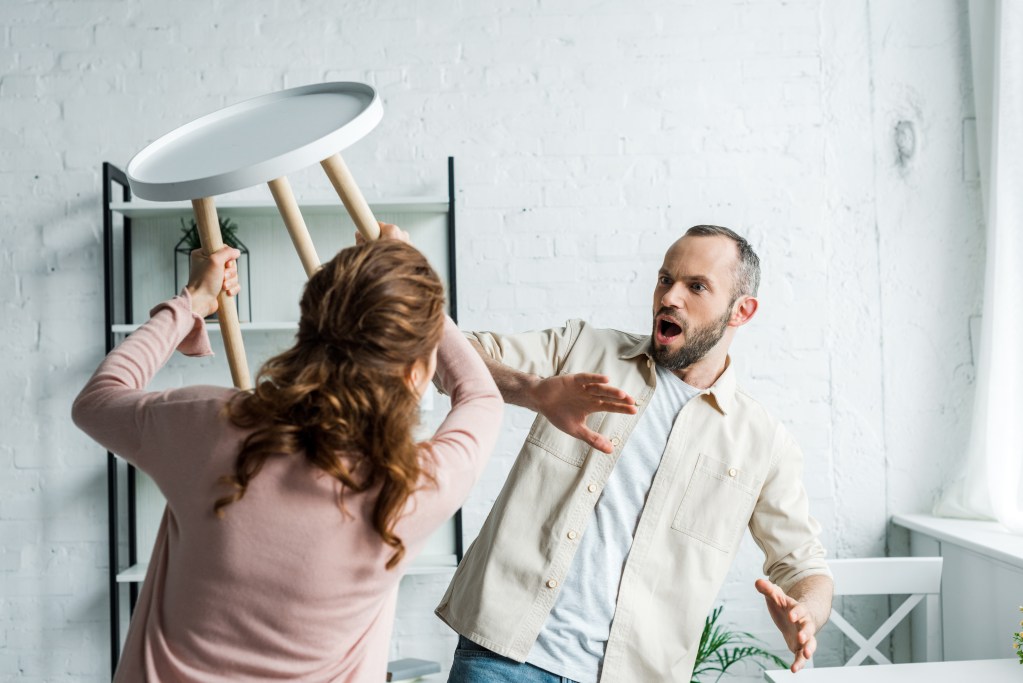 Lingering effects of abuse: angry woman holding chair while threatening man at home