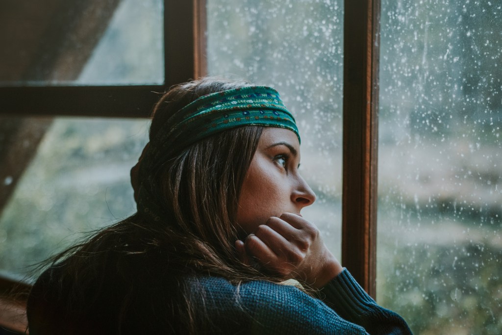 Why do I find comfort in sadness? Woman looking out of window, watching rain fall