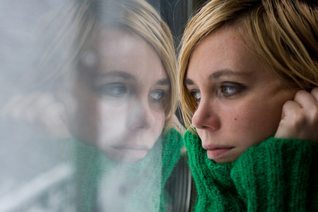 Breakthrough in Mental Health Recovery: Woman with green warm sweater reflected in a glass window looking outside