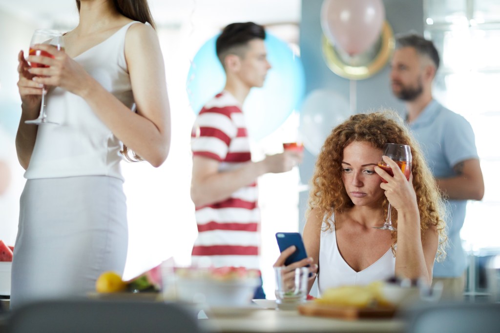 Paperclipping: Upset girl having drink by table while reading strange message in smartphone at party