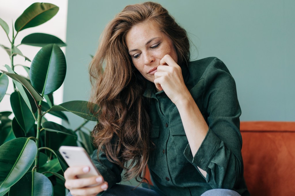 Red-haired woman looks at chat message from her AI psychologist on her mobile phone