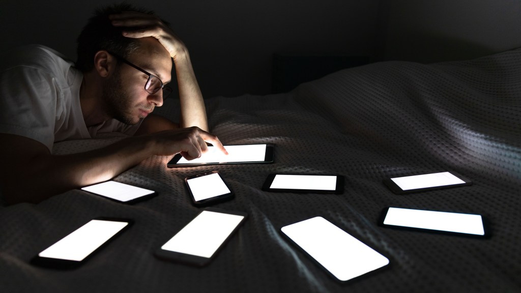 Man doom-scrolling on several devices, social media addiction, risky online behaviour