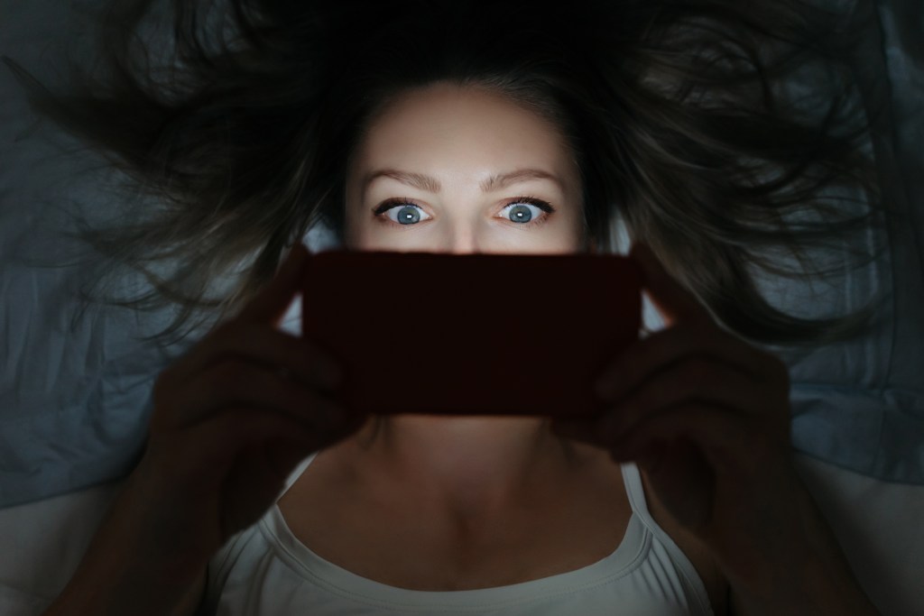 AI psychosis? Spiraling female addictively staring at her smartphone late at night in bed.