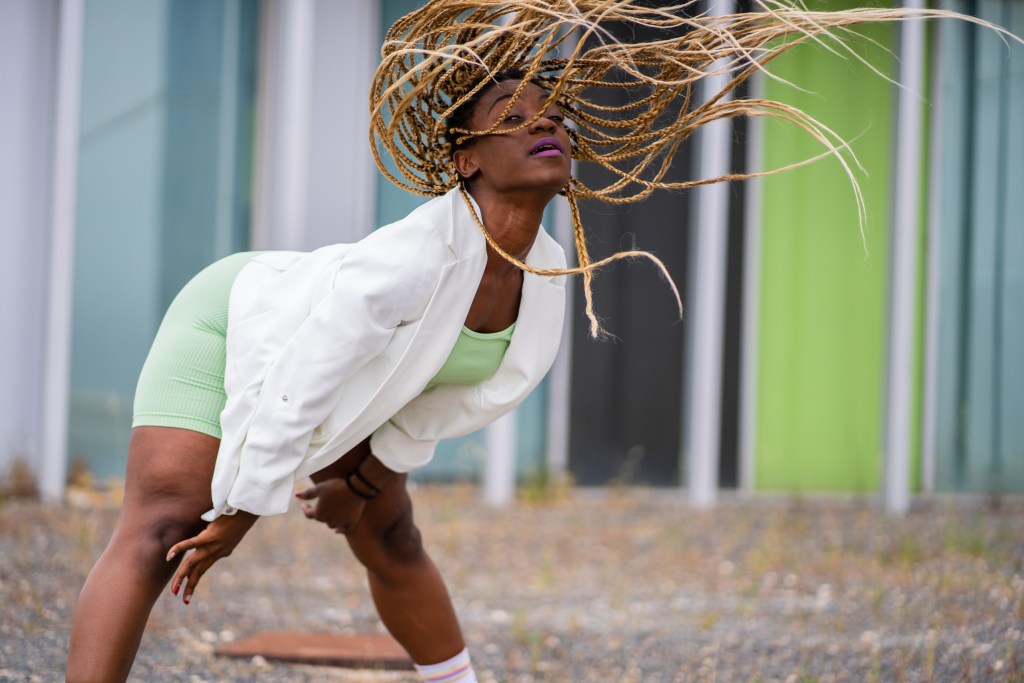 Dance it out! Black woman with braids dancing freestyle in front of a modern building