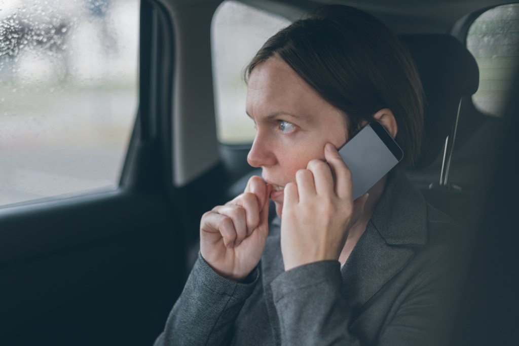 Nervous businesswoman biting nails, talking on phone, wondering how to stop worrying about things she can't control