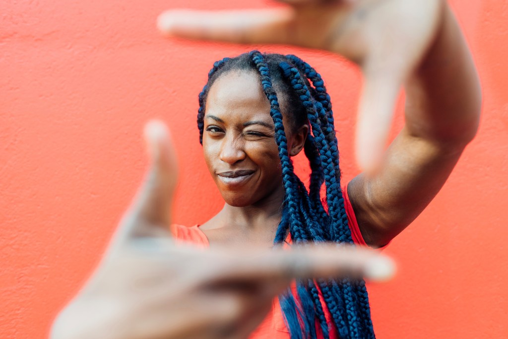 Portrait of young woman with braids making finger frame and repeating favorite daily affirmations