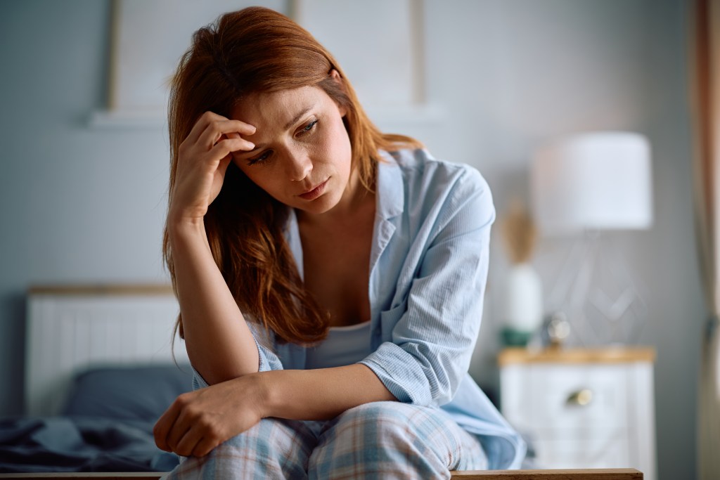 Emotional numbing: Woman sitting on her bed, holding her head in frustration.
