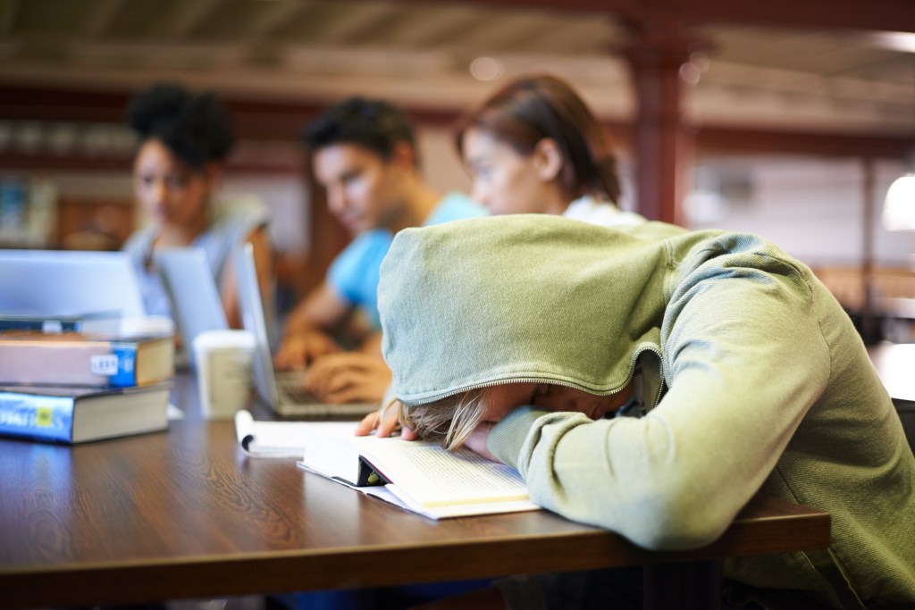 Burned out student, overwhelmed by academic stress, sleeping on his book in class