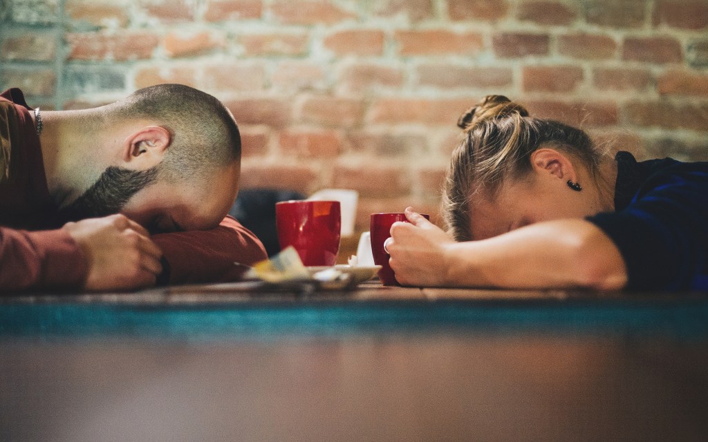 Tired workers with heads on desk, risking the effects of caffeine and anxiety 